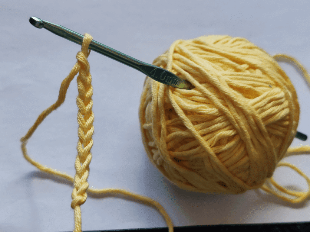 Beginner crocheter creating a simple foundation chain with blue yarn and crochet hook