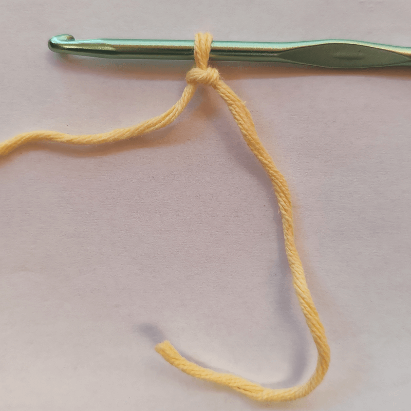 Hands forming a slip knot with yarn, first step in learning how to crochet – easy tutorial for beginners.